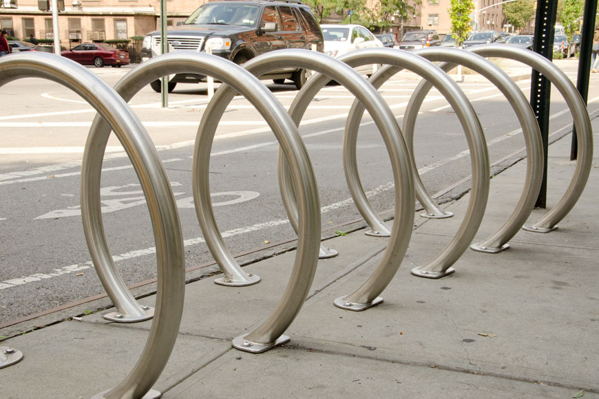 一组圆形自行车架坐落在一条繁忙街道的路边:后面是一辆模糊的汽车。