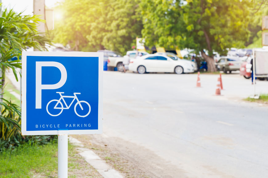 蓝色自行车停车标志站立在前景，汽车停放在背景中