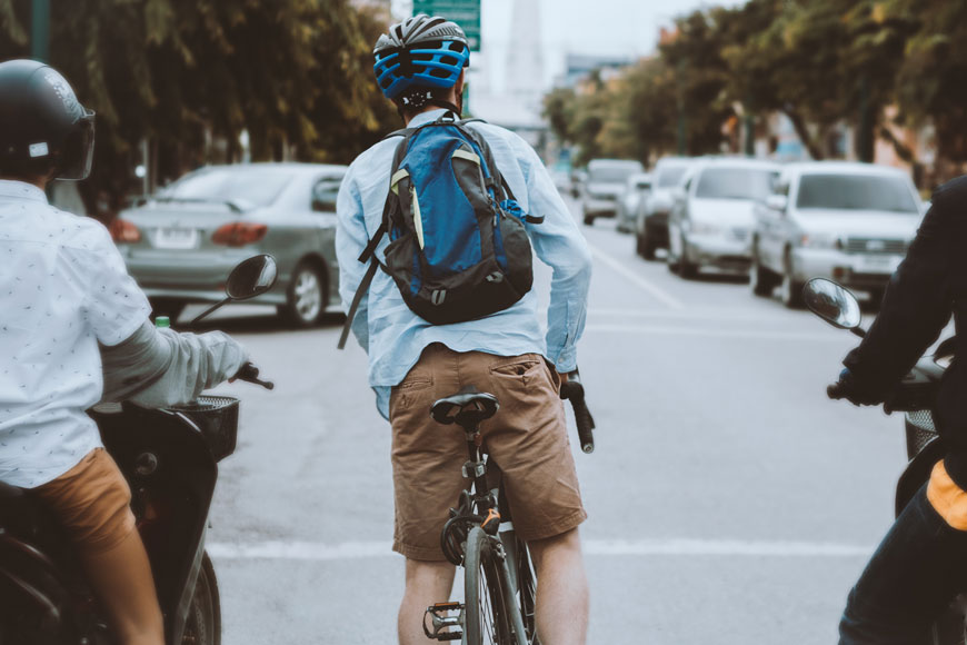 一名男子背着背包，穿着短袖蓝色牛津衫，骑着自行车等在路灯旁。