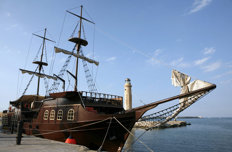 一艘棕色的“海盗船”，船桅上有帆布帆，顶部有乌鸦巢，由码头捆绑