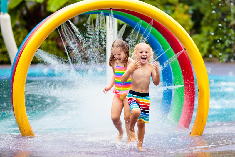 两个快乐的孩子在洒水的公园里玩，公园里到处都是五颜六色的弯管。