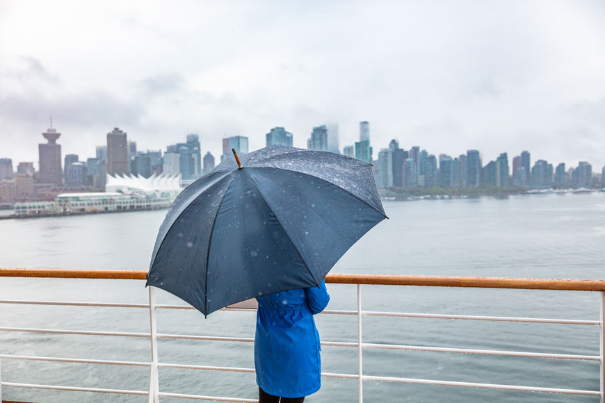 一名女子站在温哥华港口附近的一把伞下，看着游船驶入