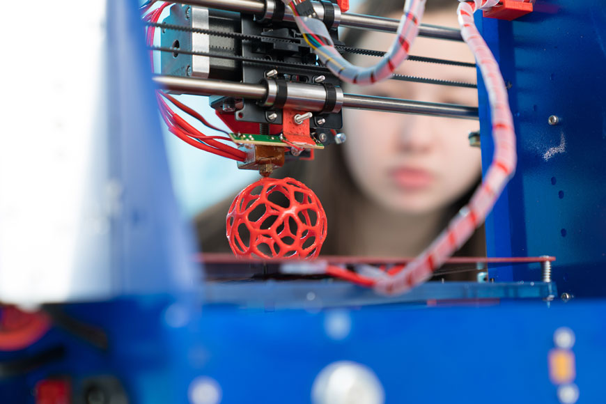一个年轻女子看着3D打印机创建球形原型