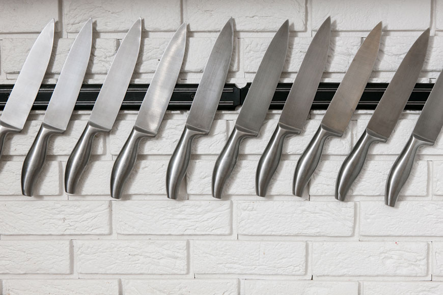 一系列厨师的刀具挂在砖墙上的磁条上涂上白色