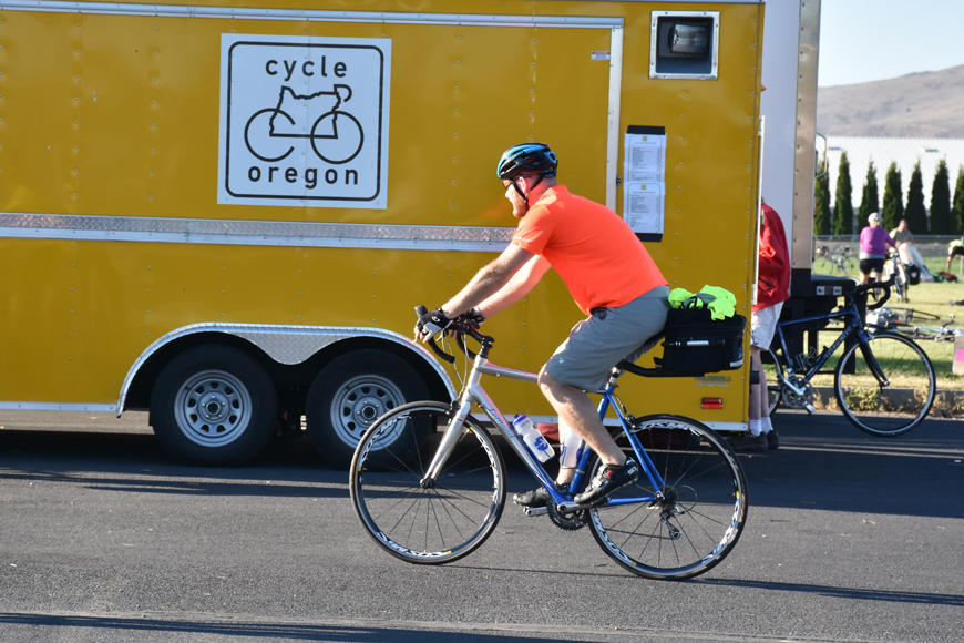 一辆写着“俄勒冈自行车”的黄色卡车停在路边;一个骑自行车的人经过它。