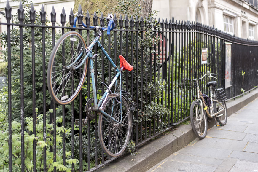 两辆自行车被锁在一道锻铁栅栏上，其中一辆被吊离人行道