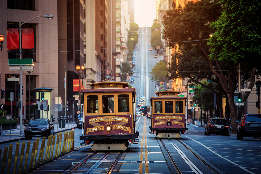 两辆旧金山手推车，红色和金色油漆沿着日出的街道旅行