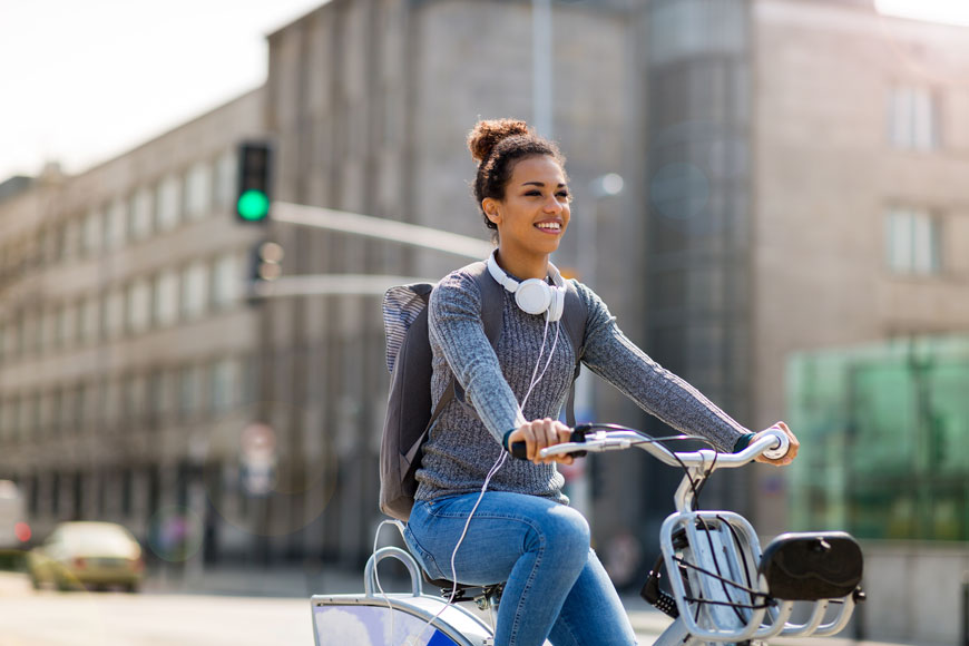 一个宽阔而引人入胜的笑容的年轻女子在城市街道上骑自行车分享自行车