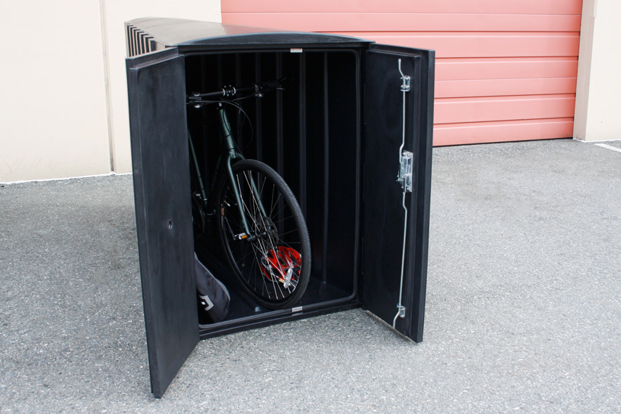 一个开放的黑色自行车储物柜包含一辆自行车，一个头盔和一个挂袋。