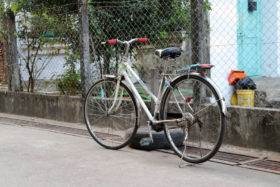 一辆自行车停在一个汽车轮胎旁，旁边的栅栏前面有一个危险的栅栏