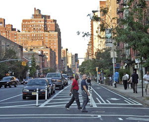 一张单向街道上的十字路口的照片，显示停放的汽车，缓冲区和纽约市的自行车道