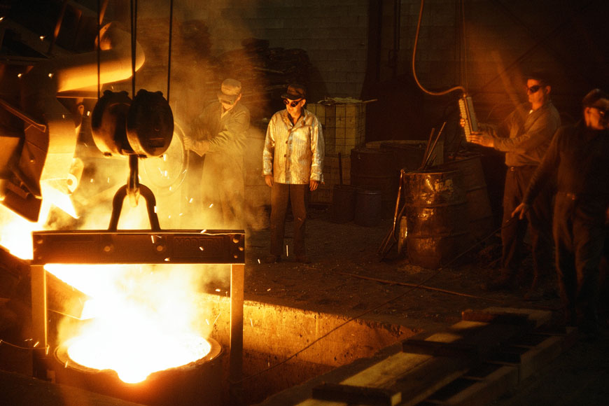 一群戴着护目镜的铸造工人站在一个装满熔化金属的勺子周围