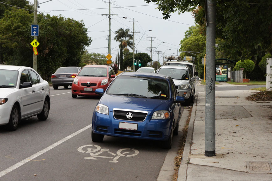 一连串停在自行车道中的汽车，前汽车在彩绘自行车图标后面