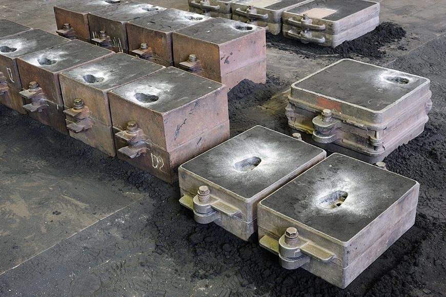 三排不同大小的铸造烧瓶坐在肮脏的铸造厂地板上，而他们的铸件冷却