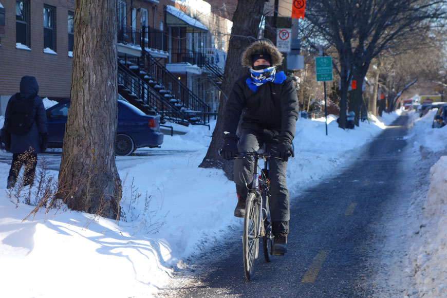 在蒙特利尔，一名穿着暖和外套和围巾的男子骑着自行车沿着一条经过犁过的咸双向自行车道行驶
