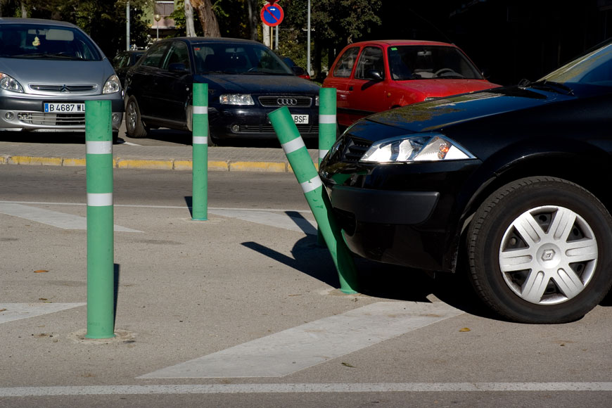 一个绿色的铺柱弯曲，因为它在停车场的黑色汽车被闪亮