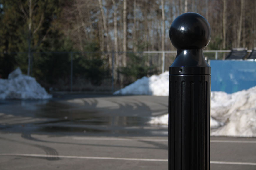 一根黑色的护柱矗立在一个满是积雪的停车场上