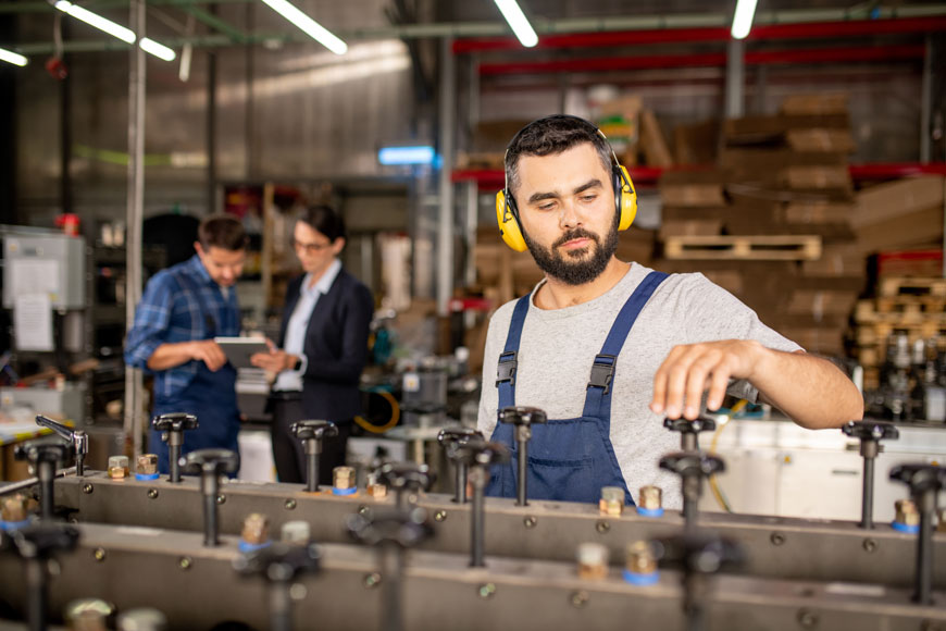 一名年轻的工人戴着耳罩在一台工业机器上工作