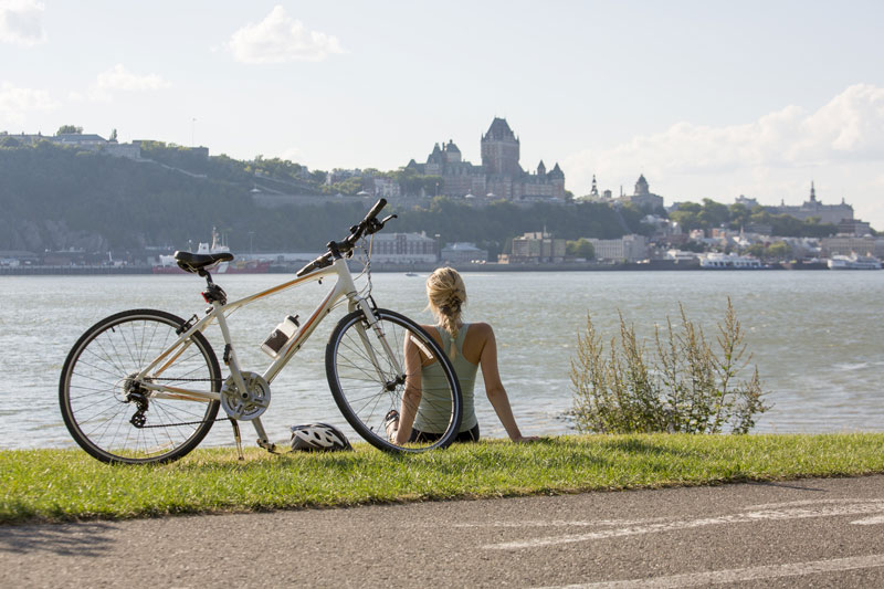 一位女士坐在自行车旁，凝视着魁北克市。