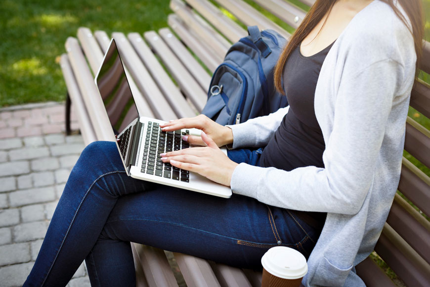 一位女士坐在长椅上，手里拿着一台笔记本电脑，旁边放着咖啡