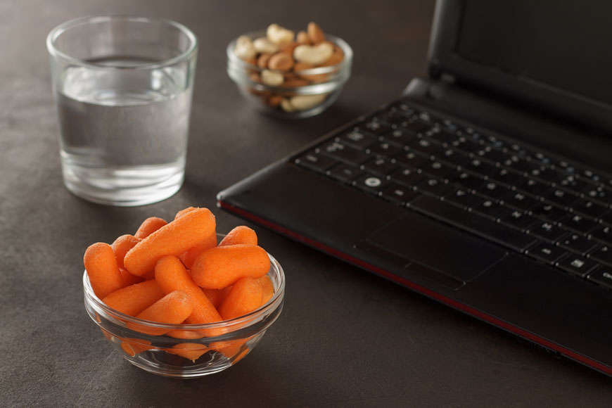 笔记本电脑的特写，一碗小胡萝卜，一碗腰果，一杯水