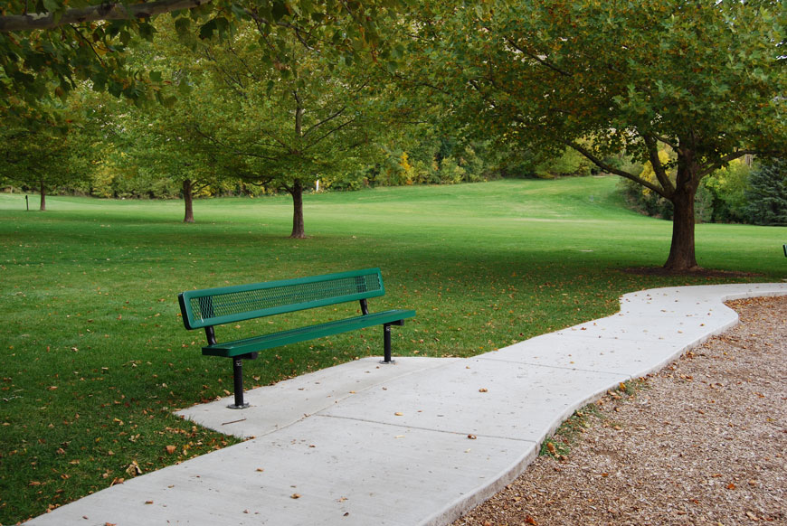 长凳由在网格样式的绿色金属坐在人行道旁边在一个象草的公园。