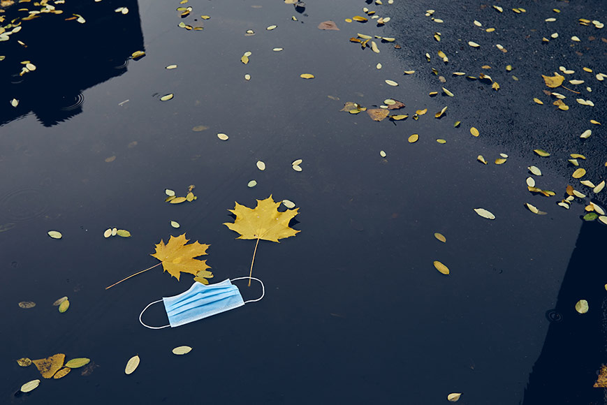 一个一次性纸制面具漂浮在水坑里，旁边是落叶