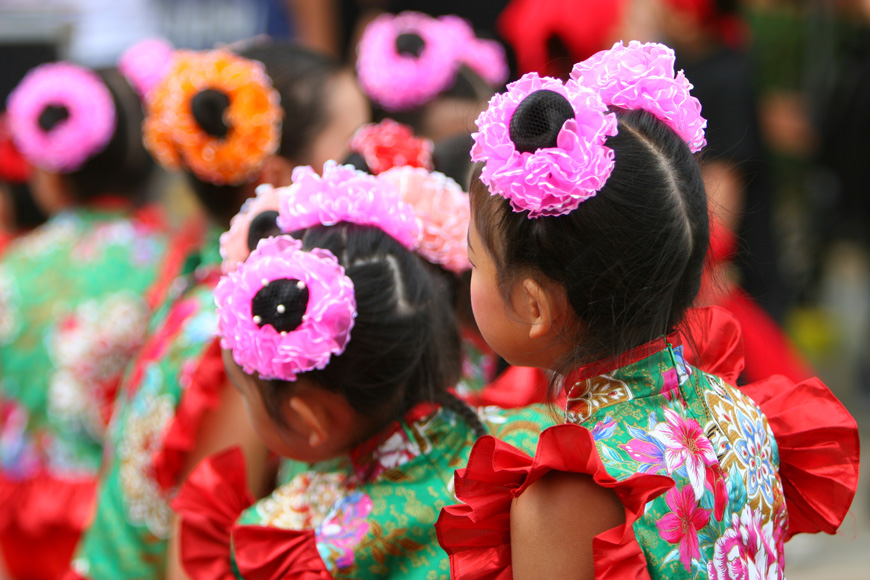 打扮成带褶皱的粉红色领带的儿童在头发上等着表演农历新年舞蹈。
