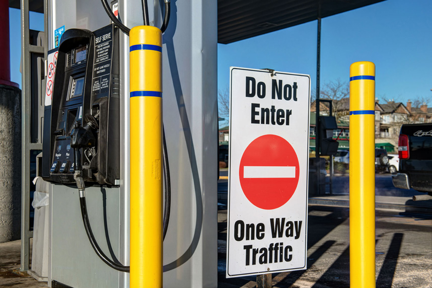 两个带有蓝色条纹的亮黄色系柱套在加油站附近的“禁止入内”标志旁边