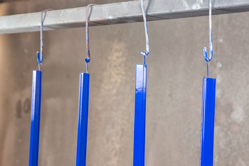 四个明亮的蓝色粉末涂层金属栏杆挂在钩子上，在固化炉中晾干