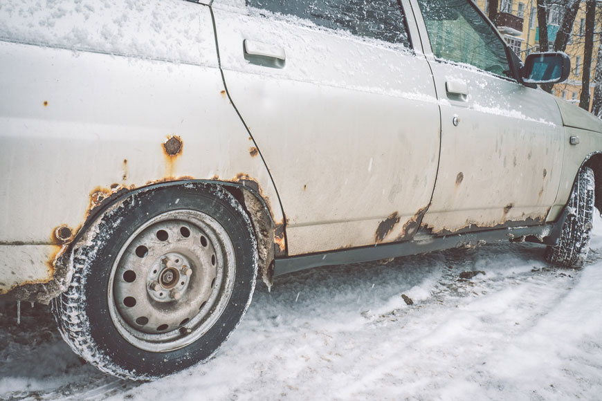 雪中锈迹斑斑的汽车侧面显示出除冰材料对钢铁的影响