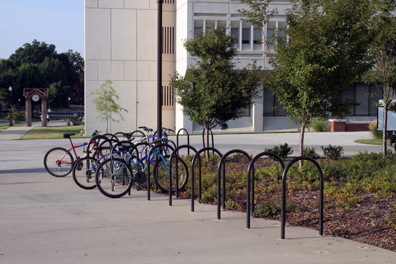 在一所学校前的灌木丛中，黑色u形架被安装成L形，几辆自行车被锁在上面