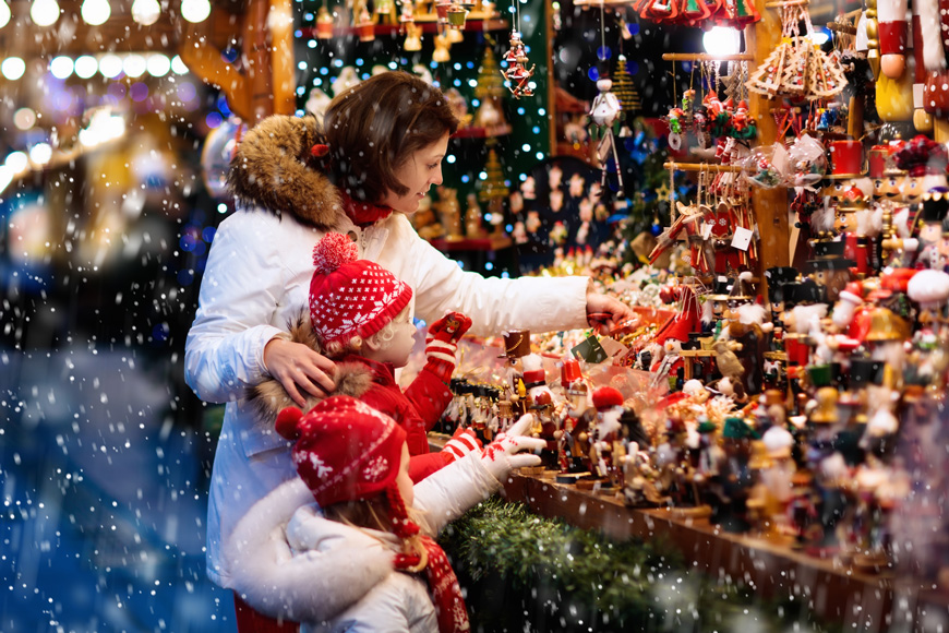一个母亲和两个孩子在雪地户外市场的摊贩看圣诞节装饰品。