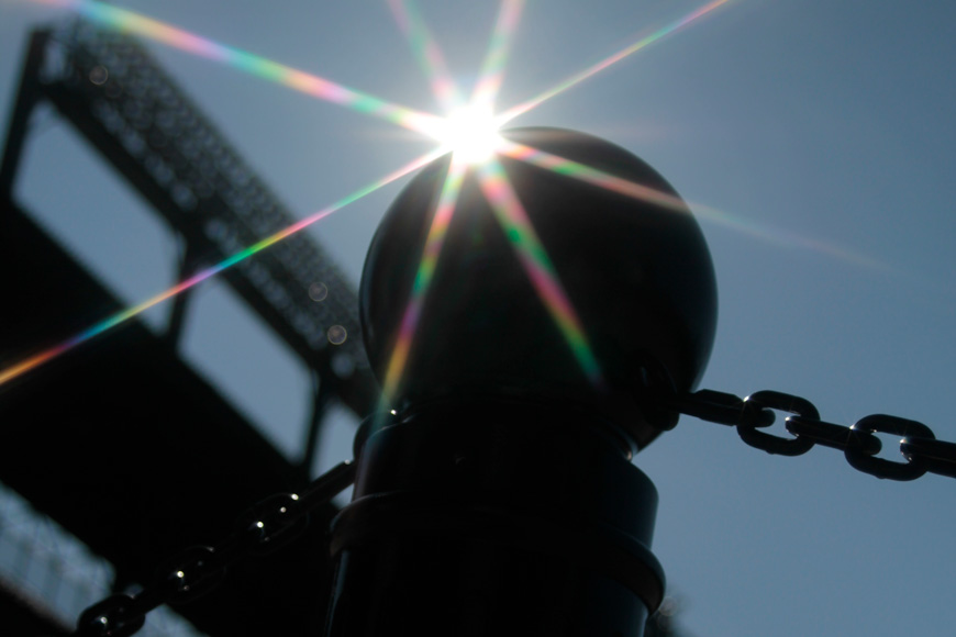 一根系柱，从地面上拍摄，在阳光下闪烁，被蓝天和棒球钻石照明框起来
