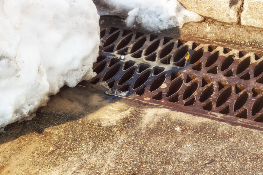一个棕色的铸铁沟渠格栅坐落在一堆雪下的路边