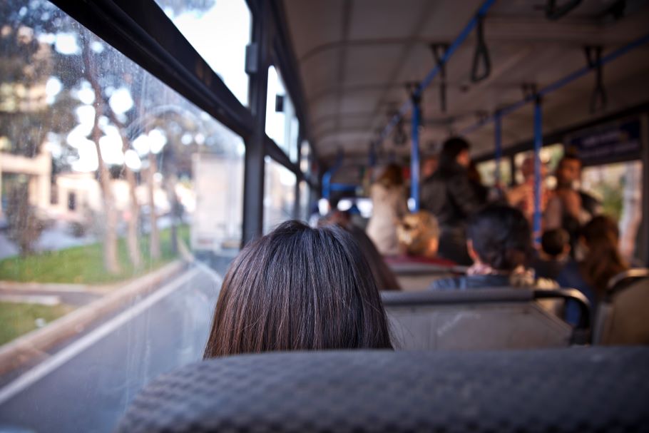 一个女人坐在公共汽车上:当她望向窗外时，我们看到了她的后脑勺。人们站在公共汽车的前部。