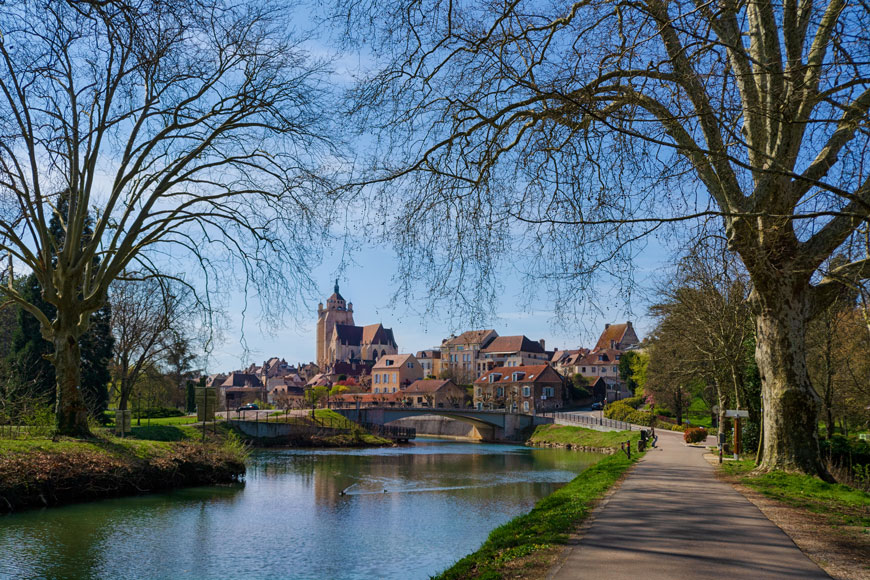 在一个古老的欧洲小镇上，一条运河延伸在一条公园小径旁，蜿蜒在一座风景优美的桥下