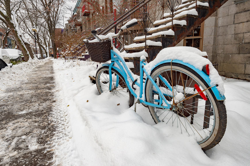 一辆被雪覆盖的蓝色自行车停在户外自行车架前